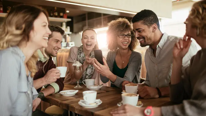 Imagen de amigos sonriendo y sentados en un café tomando café y usando un teléfono.