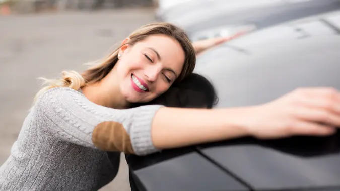 A Jolly young female driver hugging her new car.