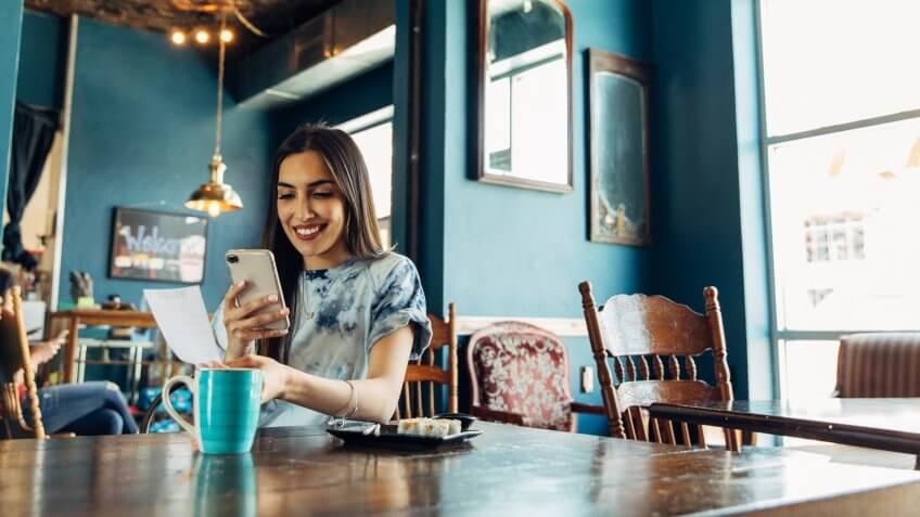 A hispanic woman of the Millennial Generation is taking a picture of a restaurant receipt after eating lunch at a local sushi restaurant.