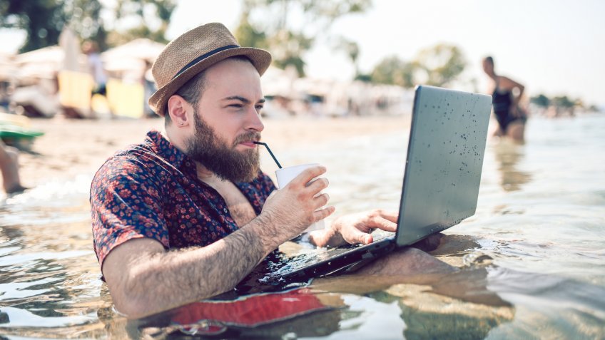 Bearded Guy With Straw Hat Watching Movie On Waterproof Laptop While Drinking Coffee In The Middle Of The Sea.