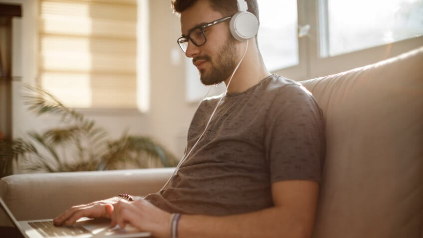 Young man using laptop and listening to music at home.