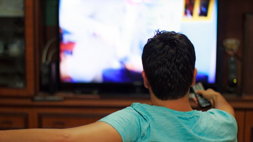 Male watching television in home living room / channel hopping.
