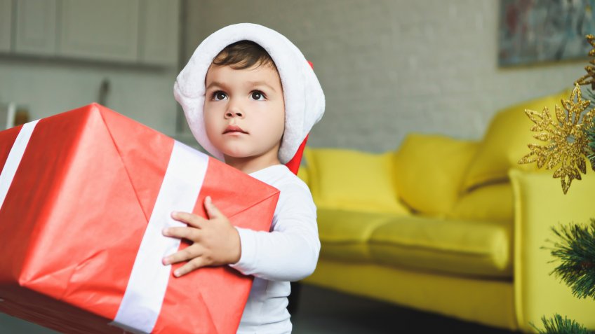 adorable boy in santa hat holding big red christmas present.