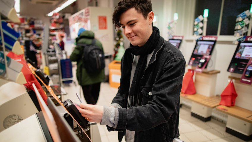 Young male adult smiling while using a self-service checkout machine while in a supermarket.