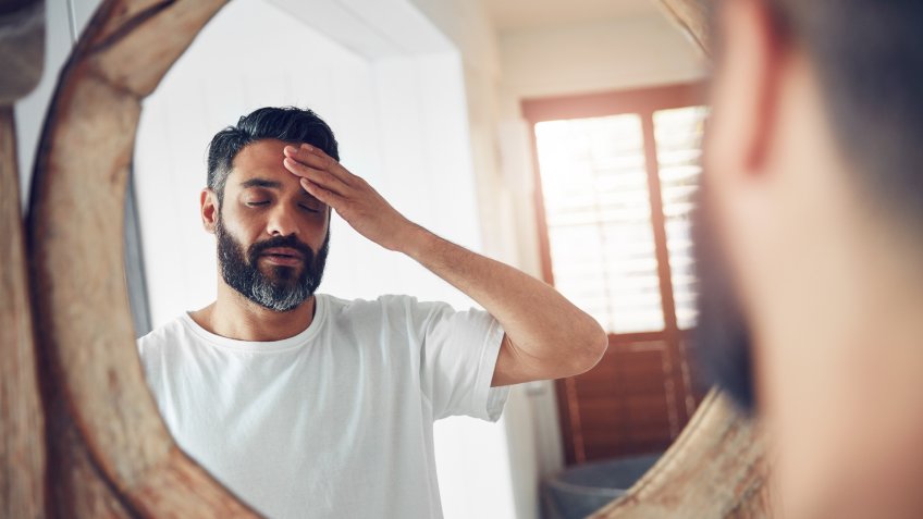 Shot of a mature man standing in front of the bathroom mirror looking exhausted.