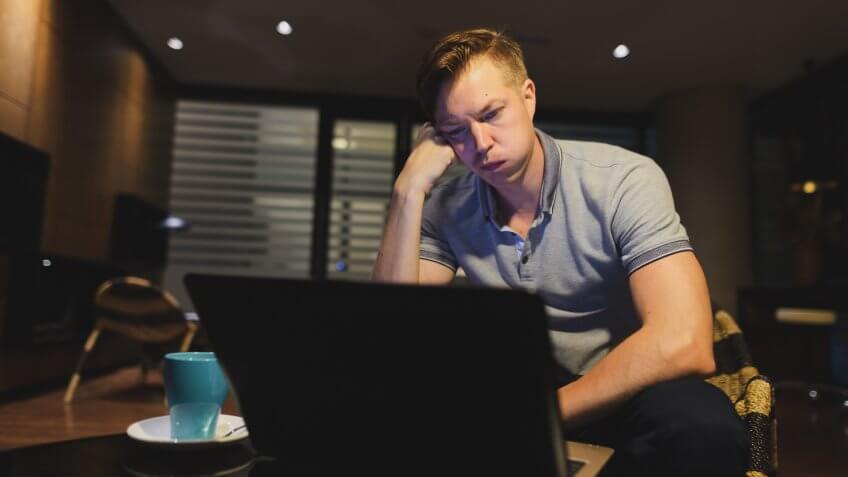 Portrait of young handsome man using laptop in the living room horizontal shot.