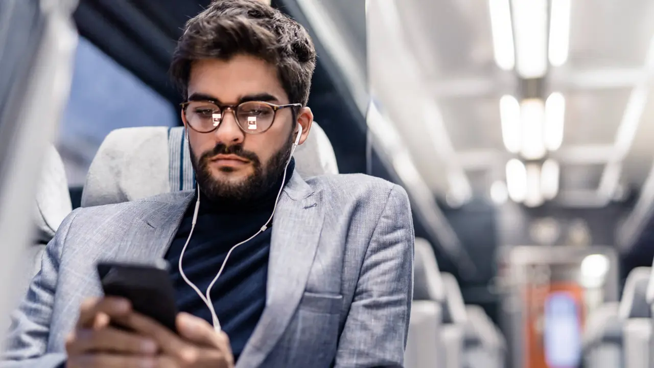 Young man reading an article on his phone and listening to podcasts while traveling by train.