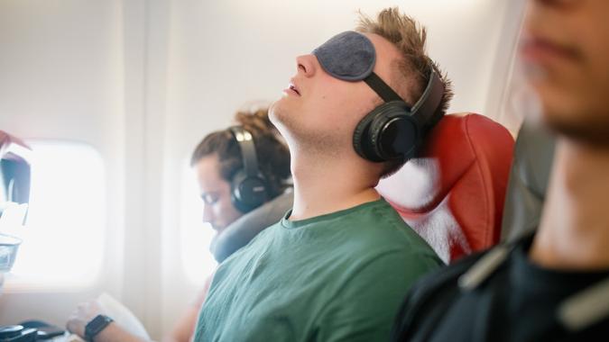 Close up shot of a young man asleep with his head back snoring on a flight in economy class.