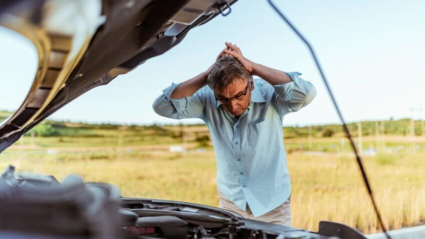 Senior Man examining a broken car on a sunny day.