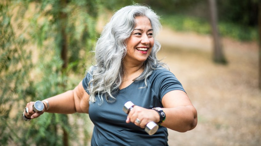 A beautiful senior Mexican Woman working out and stretching with weights.