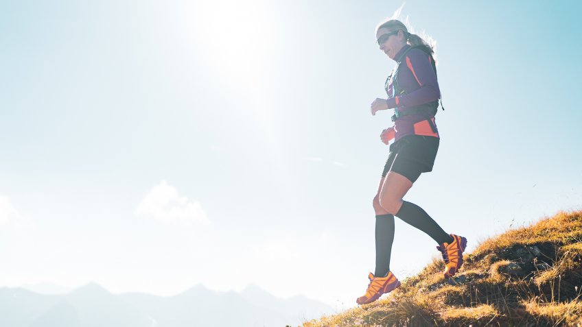 back light fit sporty 44 years old cross country trail running woman with sport compression stockings jogging down steep mountain pasture ridge high up in mountains on sunny autumn day.