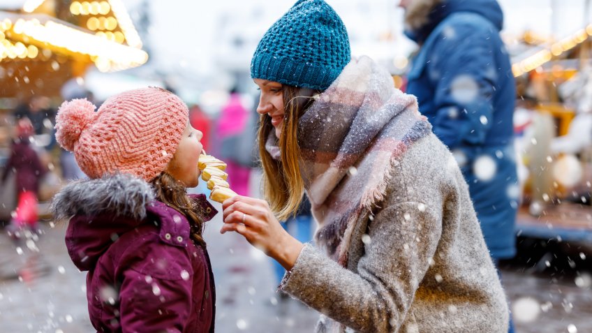 Young mother and daughter eating white chocolate covered fruits on skewer on traditional German Christmas market.