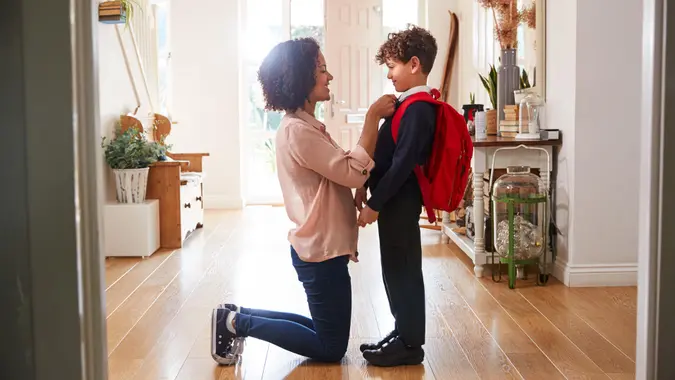 Single Mother At Home Getting Son Wearing Uniform Ready For First Day Of School.