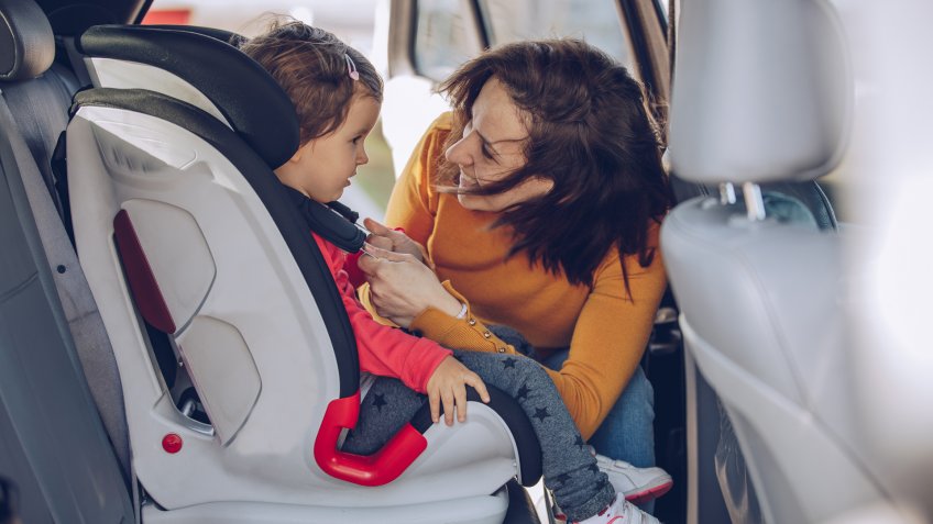 Two girls, single mother buckling up her daughter in a car, traveling together.