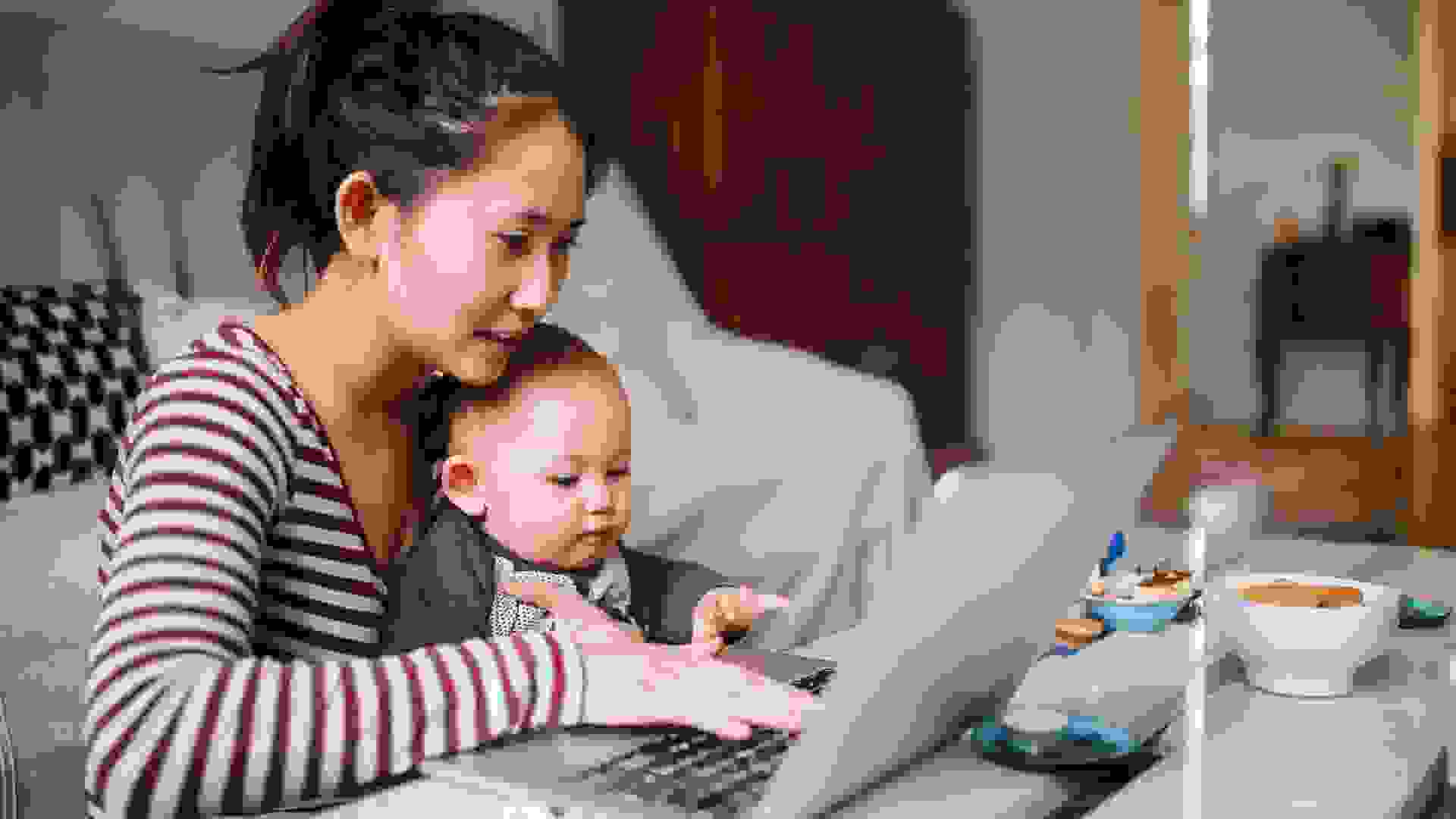 Portrait of a young Asian woman sitting at home, doing some freelance job while taking care of her little baby boy.