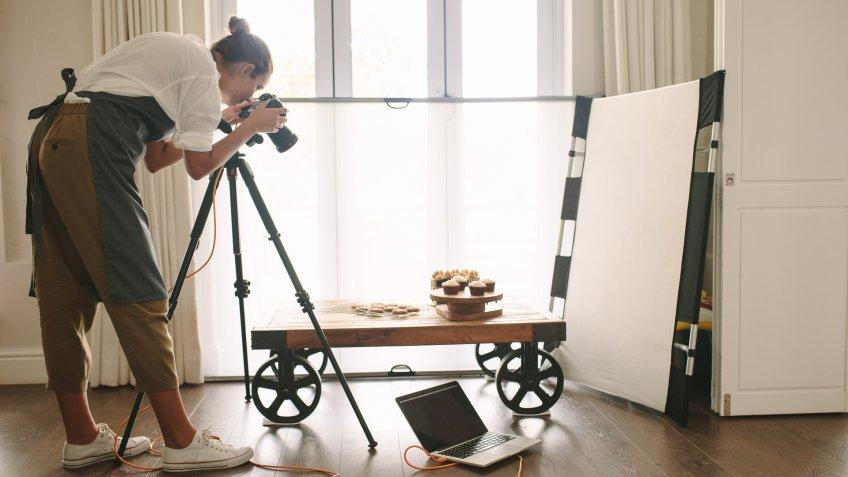 Professional food blogger taking pictures of pastry items on table with dslr camera.