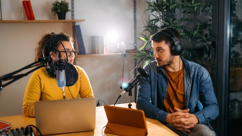 Photo of two young people recording a podcast in a studio.
