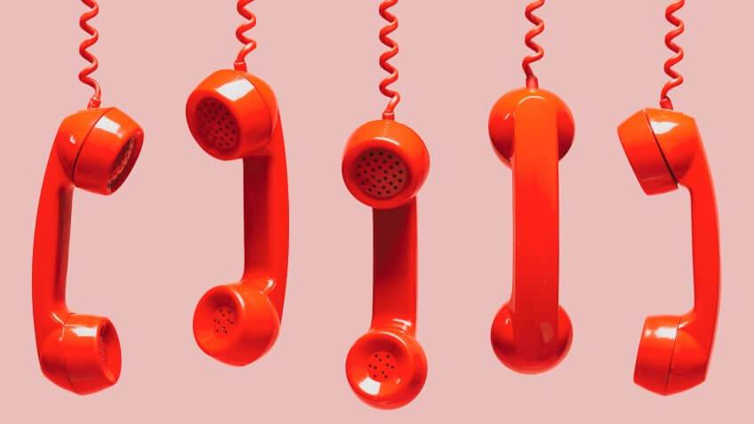 Various views of old red telephone receivers hanging on pink background with texting space, waiting for phone call, customer service concept, vintage telephone receiver.