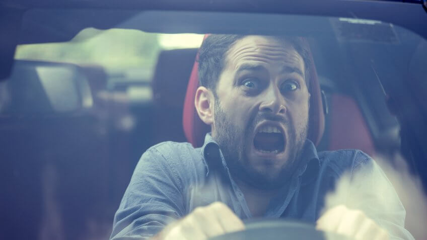 Young man driving a car shocked about to have traffic accident, windshield view.