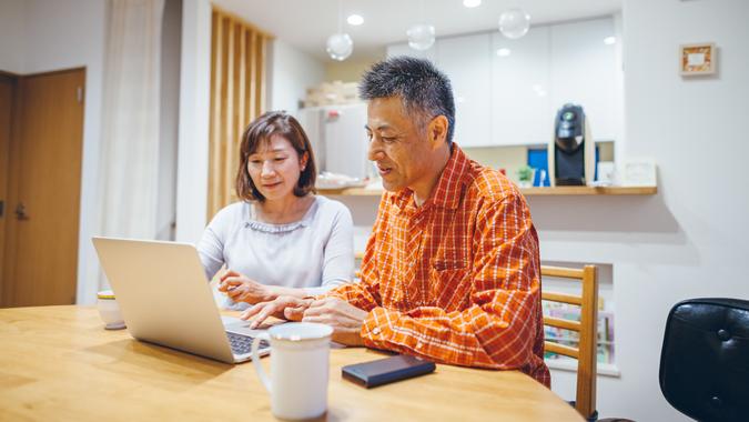 A married senior couple is using laptop at home.