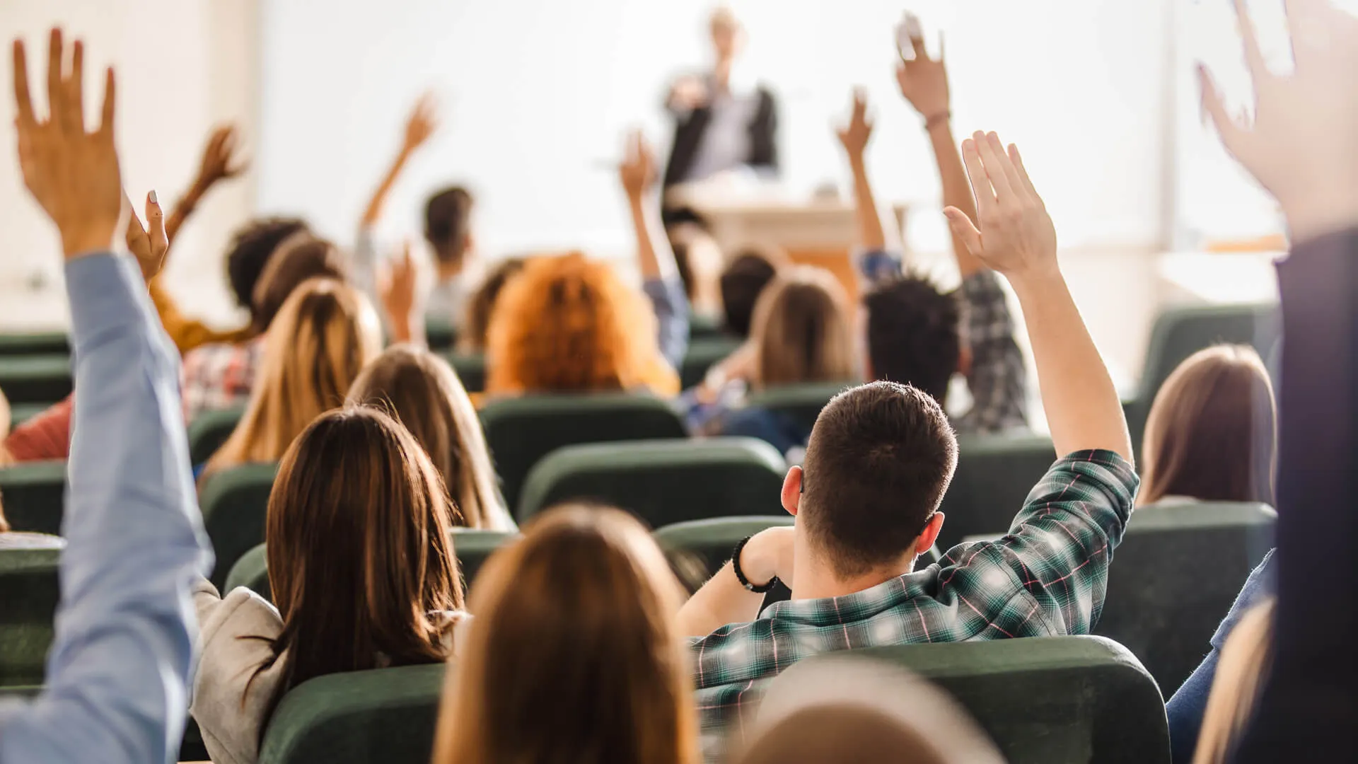 Back view of college students raising their arms on a class at lecture hall.