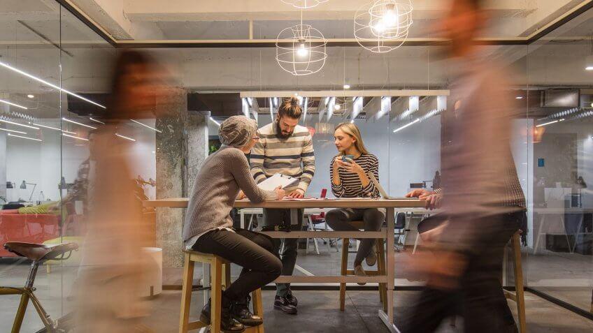 Young entrepreneur having a business meeting inside of an office while their colleagues are walking in blurred motion.