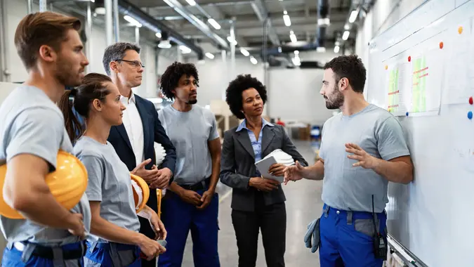 Young factory worker holding presentation about production development to company managers and his coworkers.