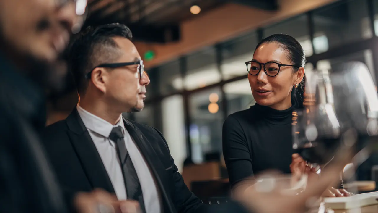 Three people—two men and one woman—are seated at a restaurant table engaged in a professional business meeting.