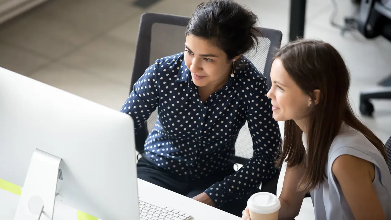 Shot of two colleagues having a coffee break together while sitting at desk discussing finances