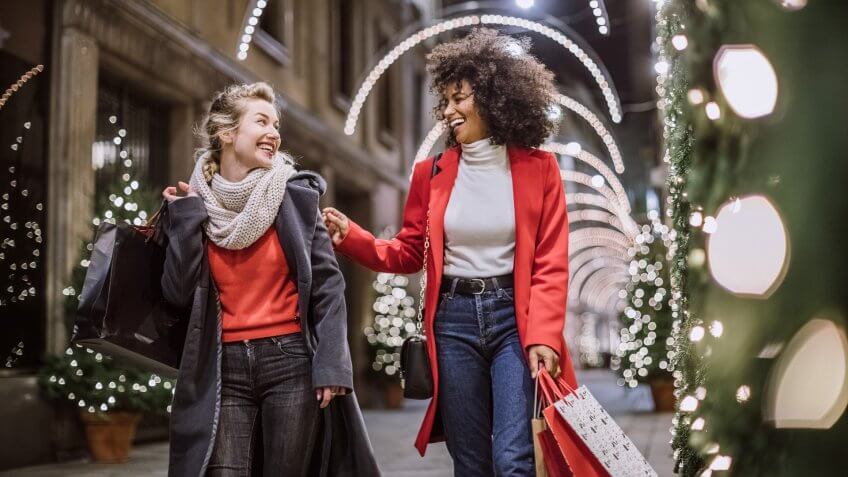 Pretty Young Female Friends Smiling Broadly In Cheerful Manner Having Fun At Shopping Mall, Buying Christmas Gifts.