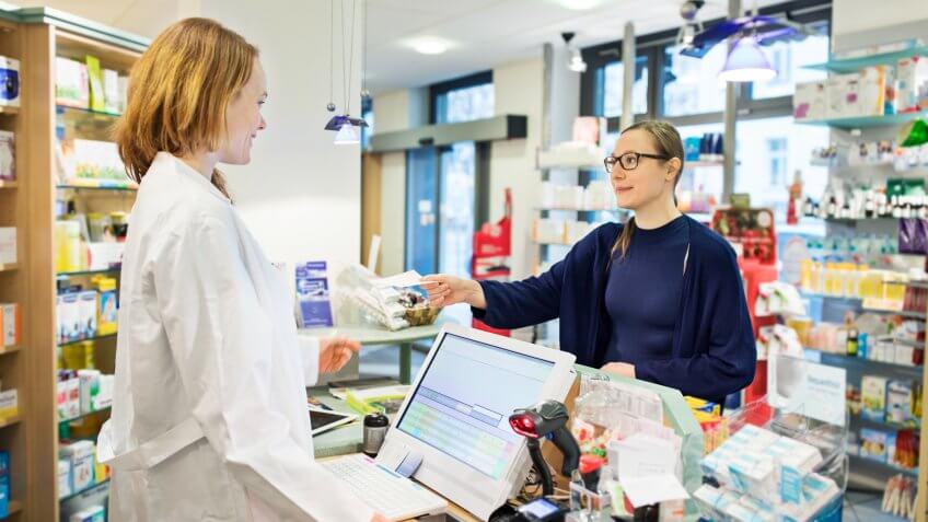 Woman giving prescription to female pharmacist in store.