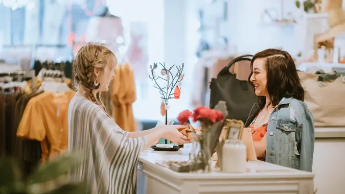 A fashionable Hispanic woman works in her small retail clothing store, selling new fashion items.