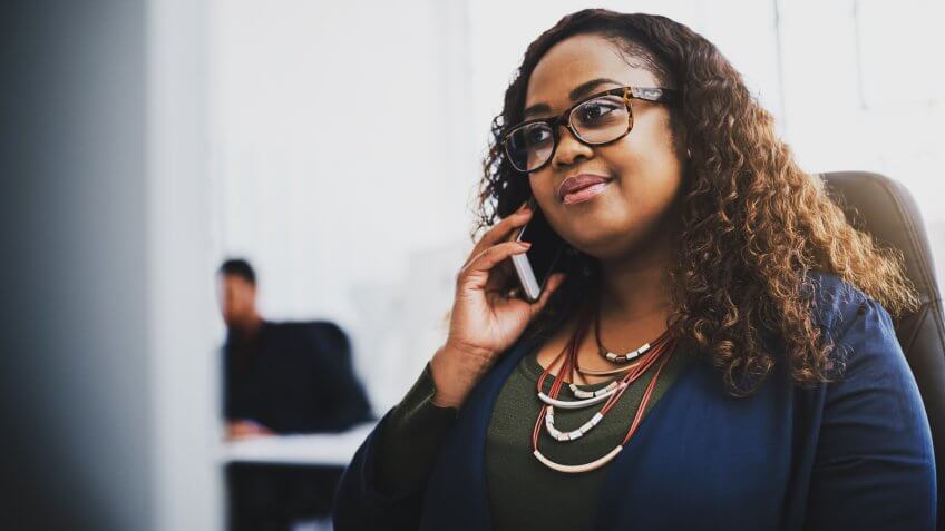 Shot of a young businesswoman using a mobile phone at her desk in a modern office.