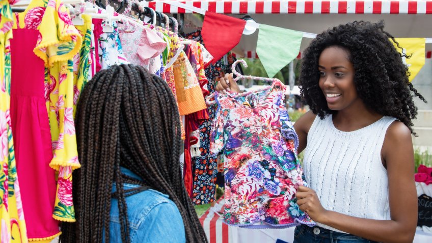 African american woman presenting colorful clothes outdoors at typical traditional market.