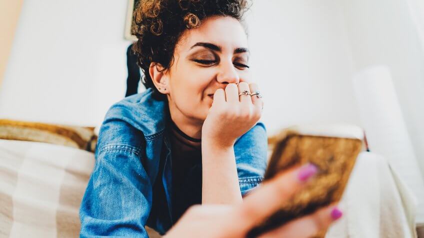 Young woman, with short, curly hair, using phone, in her apartment, lying upside down.