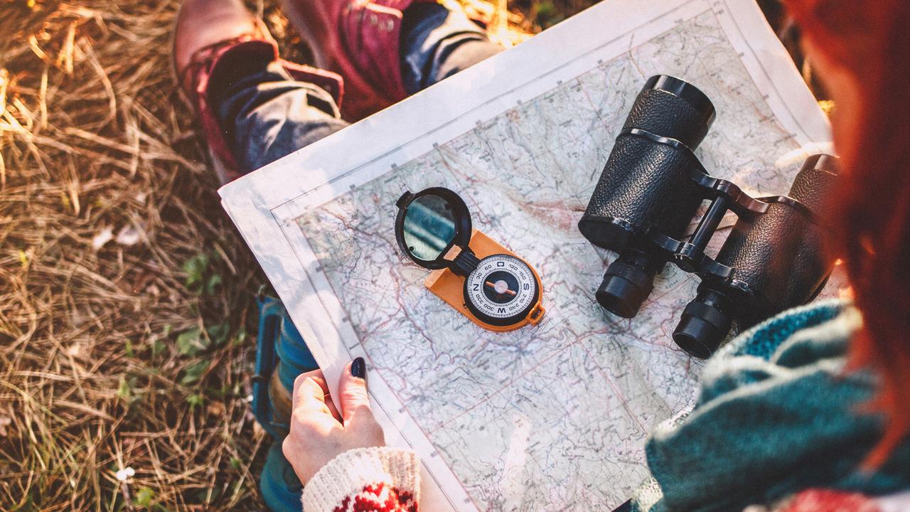 Traveler young woman searching direction with a compass on background of map in the forest.
