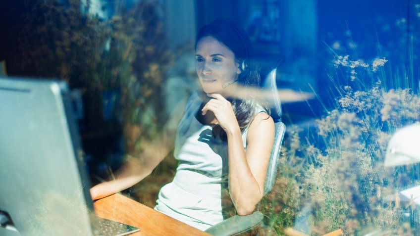Businesswoman with headset working at computer in sunny home office.