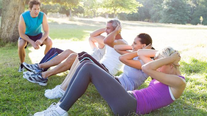 people exercising in park with trainer