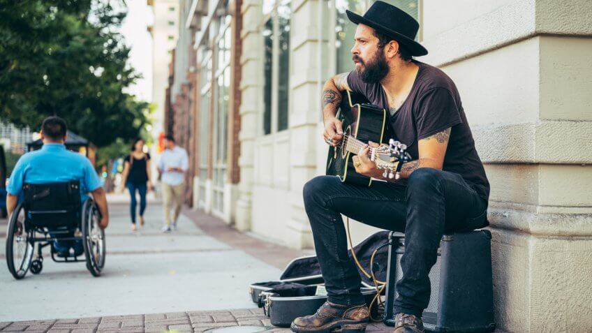 A busker street musician playing music for tips on a city sidewalk.