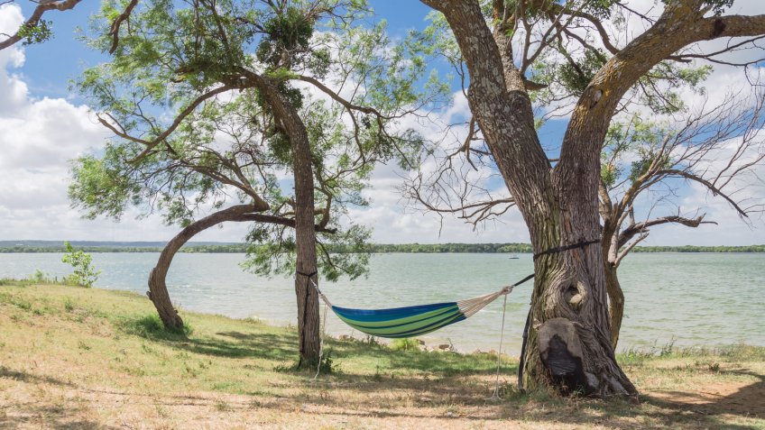 Empty green hammock in shade tree shades at lakeside park in Grand Prairie, Texas, USA.