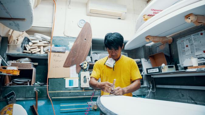 Mature man making and shaping a surfboard in his small business surf shop.