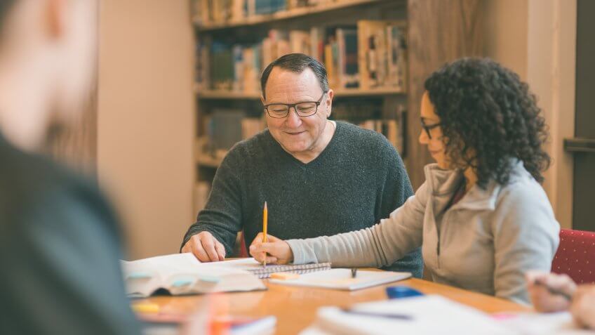 Professor works with group of college students in library at a study table.
