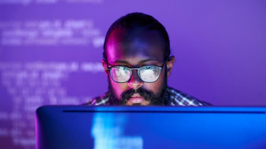 Young serious programmer in eyeglasses concentrating on working with coded data on computer screen.