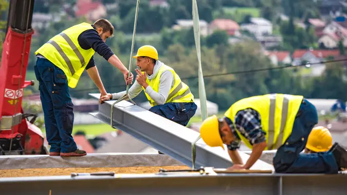 Shot of construction workers working on a girder of a prefab home, focus on foreground.