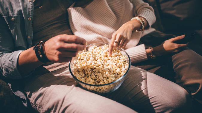 Elegant couple watching movie together and eating popcorn Close-up of chic couple's hands watching television and eating popcorn at night.