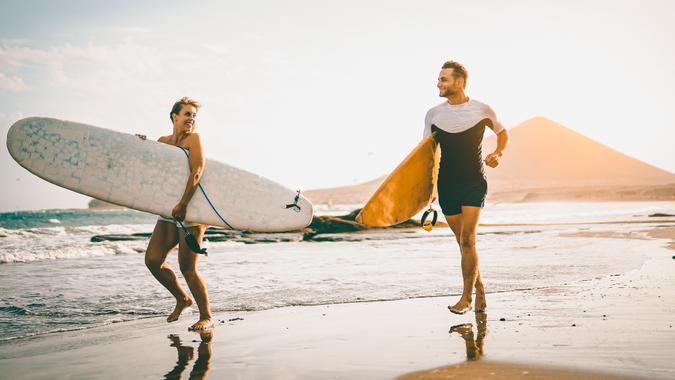 Young couple of surfers running with surfboards on the beach at sunset - Happy lovers going to surf together - People, sport and lifestyle concept - Vintage filter - Focus on woman board.
