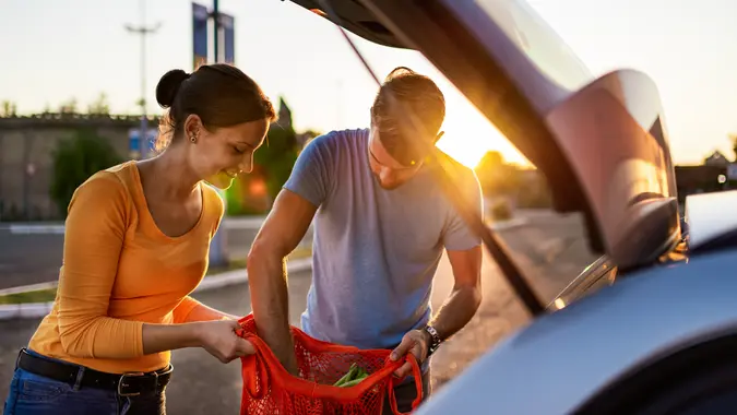 Young couple after grocery shopping on parking lot, putting groceries in car trunk.