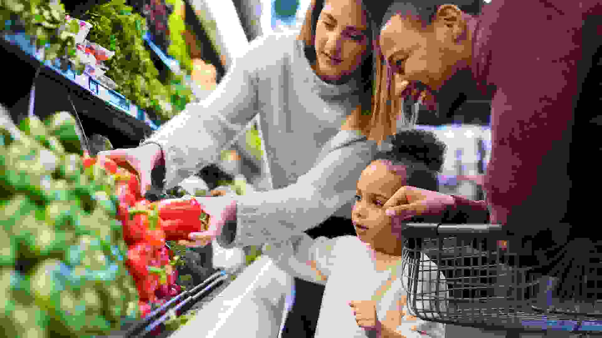 A pre-school age girl helps her parents pick out veggies in the produce section at the grocery store.
