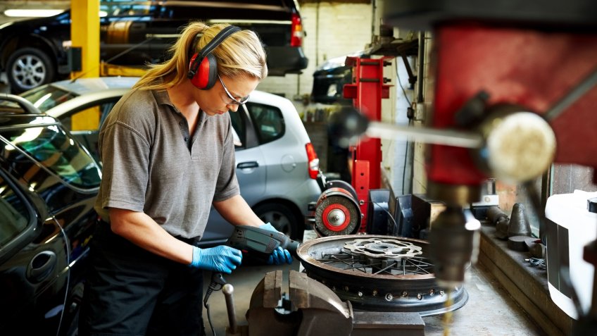 Female mechanic working on car rims in auto garage.