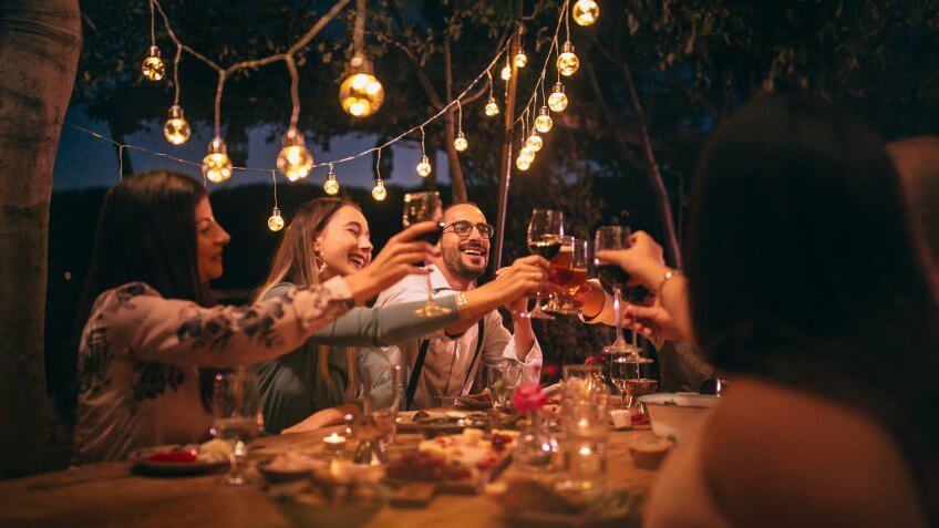 Happy young friends having fun and toasting around mediterranean dinner party table in Italian countryside.